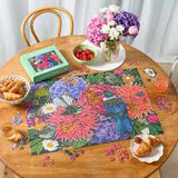 Floral puzzle on a wooden table with a box, flowers, and pastries.