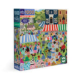A 1000-piece jigsaw puzzle box featuring a colorful, busy illustrated street market scene with many people, tents, and buildings. The box shows the brand 'Puzzle Baron' and a circular 'Organic' logo on the front and spine.