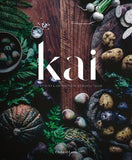 Cover of the book 'Kai' featuring a wooden table topped with an array of fresh food items like fruits, vegetables, and possibly some prepared dishes, with the title 'kai' displayed prominently.